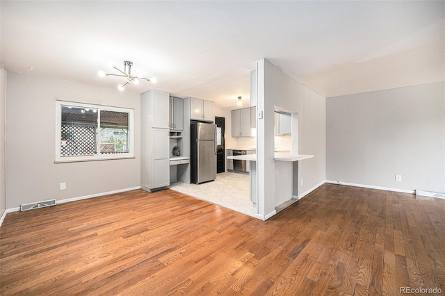 unfurnished living room with baseboards, a notable chandelier, light wood-style flooring, and visible vents