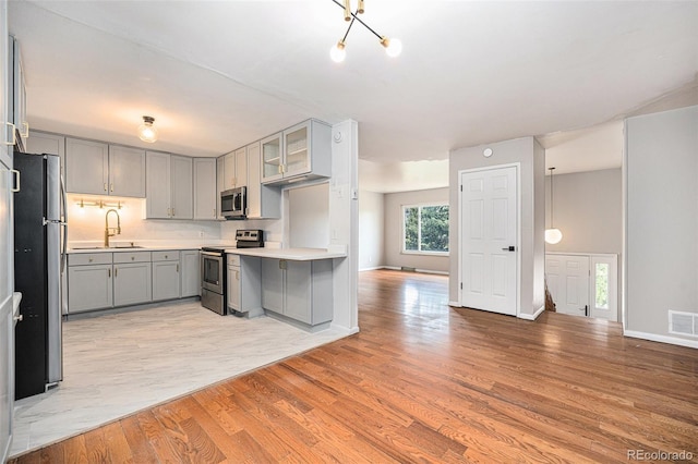 kitchen with appliances with stainless steel finishes, a sink, light wood-style floors, light countertops, and gray cabinets