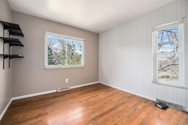 empty room featuring baseboards, wood finished floors, visible vents, and wallpapered walls