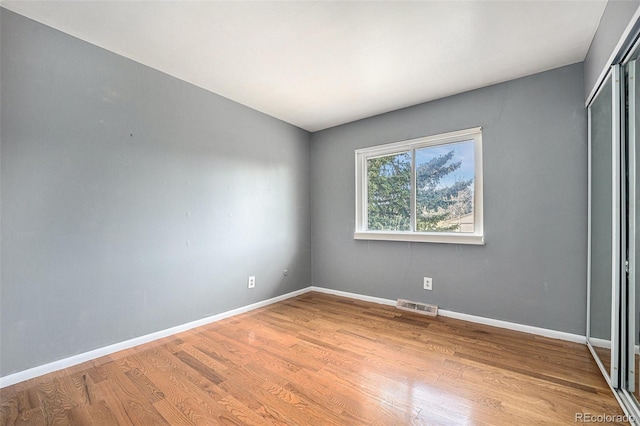 unfurnished bedroom featuring baseboards, a closet, wood finished floors, and visible vents