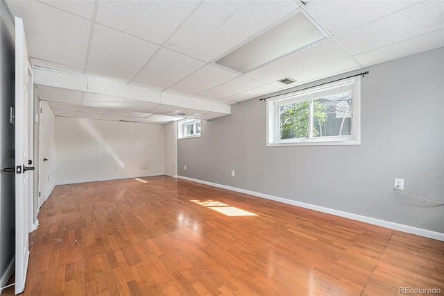 basement featuring visible vents, baseboards, a drop ceiling, and wood finished floors