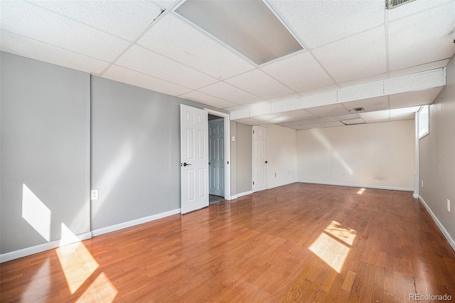below grade area with baseboards, a drop ceiling, and wood finished floors