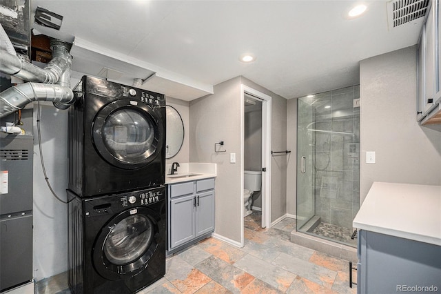 clothes washing area featuring visible vents, a sink, baseboards, stacked washer and clothes dryer, and recessed lighting