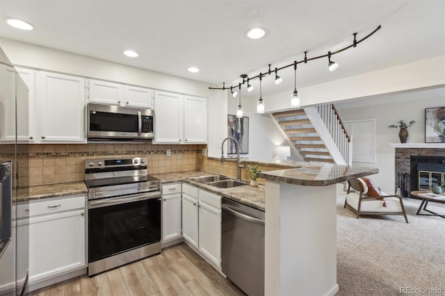 kitchen featuring a sink, a peninsula, stainless steel appliances, white cabinets, and decorative backsplash