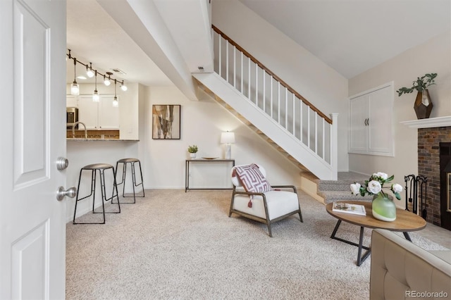 living area with baseboards, carpet floors, stairway, and a brick fireplace