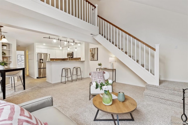 living area featuring baseboards, a high ceiling, stairway, and light colored carpet