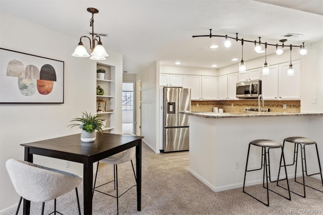 kitchen featuring white cabinetry, tasteful backsplash, a peninsula, stainless steel appliances, and visible vents