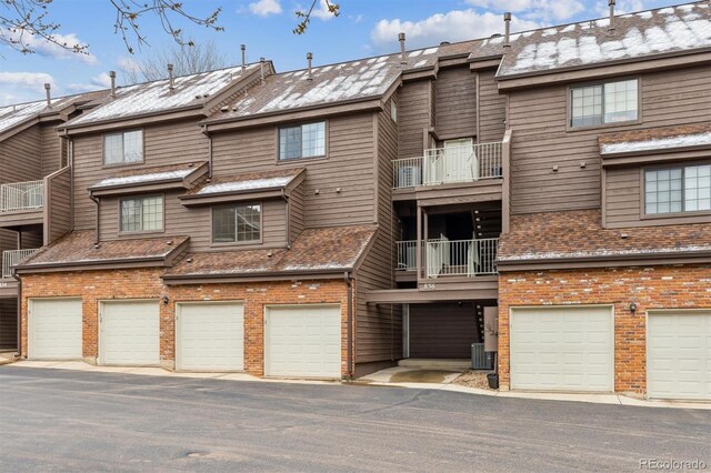 view of front of house featuring brick siding, a balcony, central air condition unit, and an attached garage