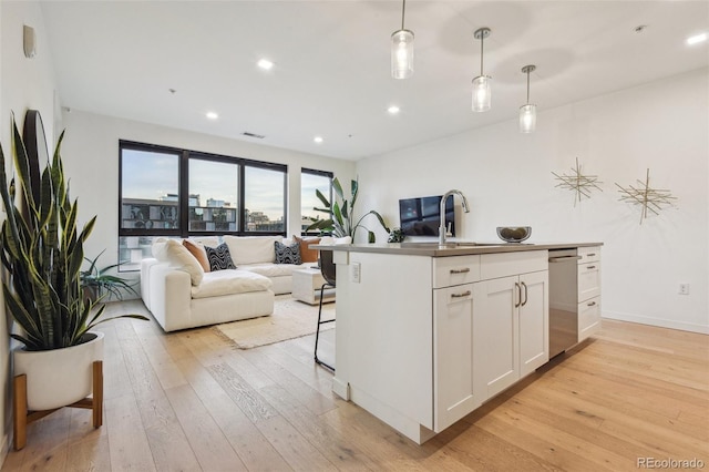 kitchen with white cabinets, light hardwood / wood-style floors, hanging light fixtures, and an island with sink