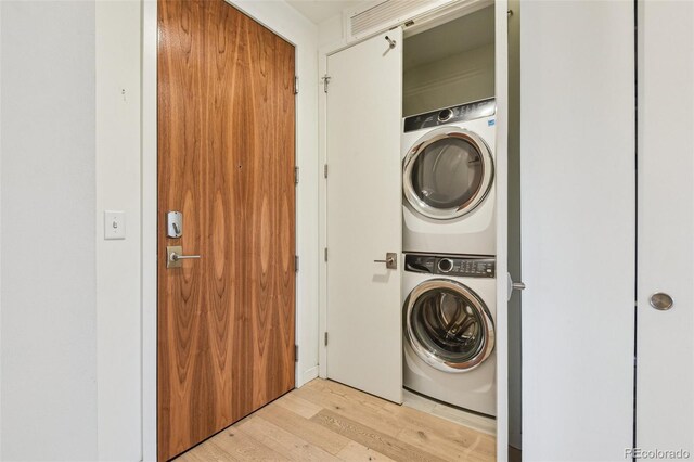 laundry room featuring laundry area, stacked washer and dryer, and light wood-style floors