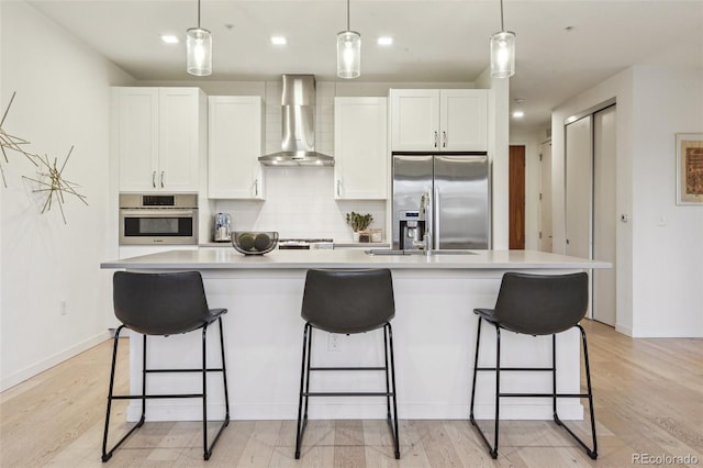 kitchen featuring a center island with sink, a breakfast bar area, tasteful backsplash, appliances with stainless steel finishes, and wall chimney range hood