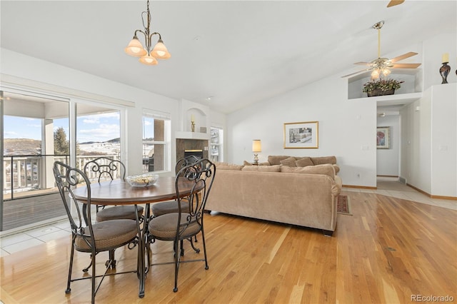 dining room with ceiling fan with notable chandelier, a fireplace, vaulted ceiling, and light hardwood / wood-style flooring