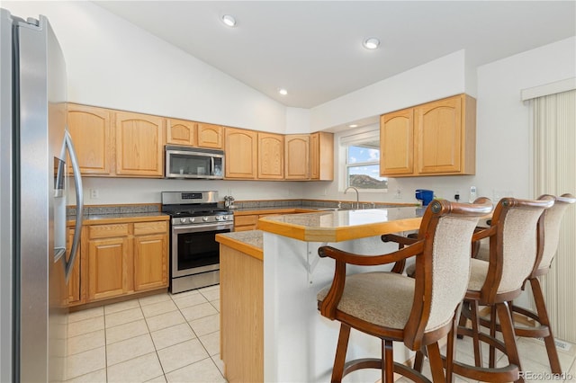 kitchen with light tile patterned floors, lofted ceiling, appliances with stainless steel finishes, a kitchen breakfast bar, and light brown cabinets