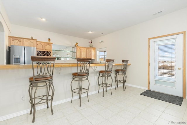 kitchen featuring stainless steel refrigerator with ice dispenser, light brown cabinetry, a breakfast bar, and kitchen peninsula