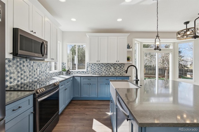 kitchen with white cabinets, open shelves, appliances with stainless steel finishes, a center island with sink, and blue cabinetry