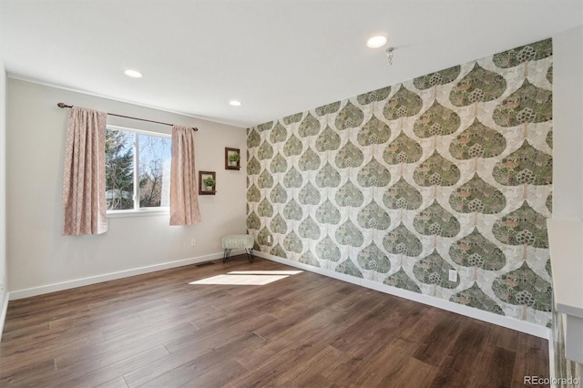 spare room with an accent wall, recessed lighting, wood finished floors, wallpapered walls, and baseboards