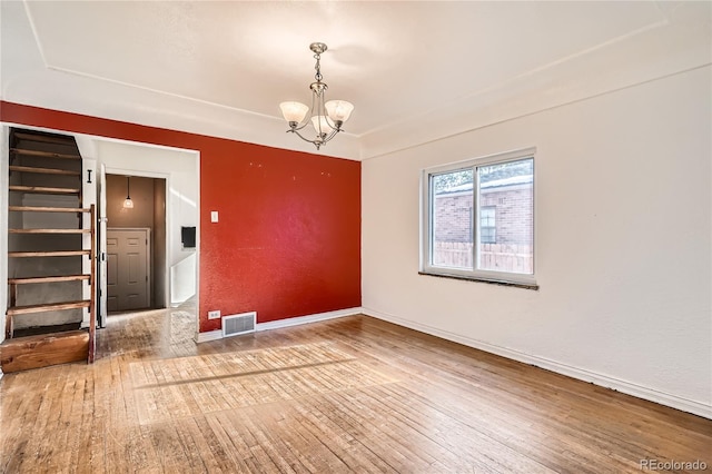 empty room with hardwood / wood-style floors and a notable chandelier