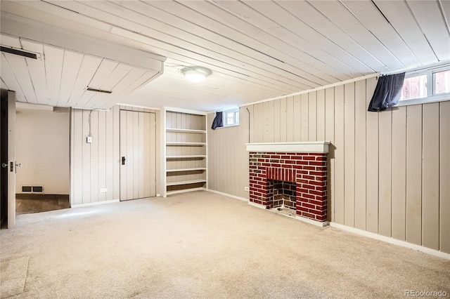 basement with carpet, wood walls, a wealth of natural light, and a brick fireplace