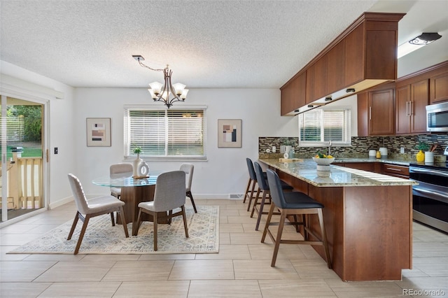 kitchen with kitchen peninsula, appliances with stainless steel finishes, light stone countertops, decorative light fixtures, and a chandelier