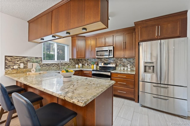 kitchen featuring a kitchen breakfast bar, kitchen peninsula, light stone countertops, and appliances with stainless steel finishes