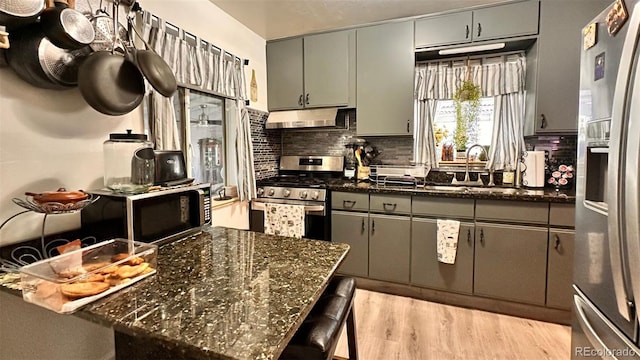 kitchen featuring backsplash, appliances with stainless steel finishes, a breakfast bar, dark stone counters, and light wood-type flooring