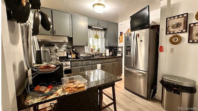 kitchen with stainless steel appliances, dark stone counters, gray cabinets, light hardwood / wood-style floors, and tasteful backsplash