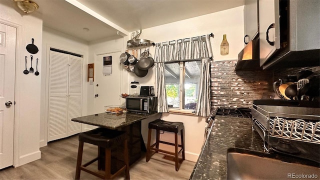 kitchen featuring a breakfast bar area, decorative backsplash, hardwood / wood-style flooring, and dark stone countertops