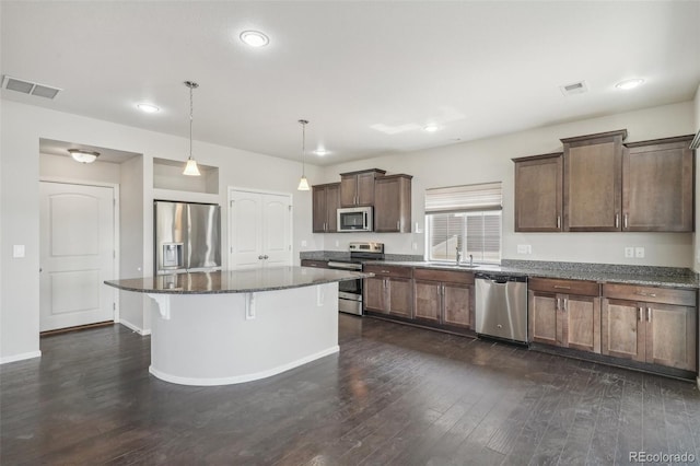 kitchen featuring a center island, dark wood-type flooring, stainless steel appliances, dark stone counters, and decorative light fixtures