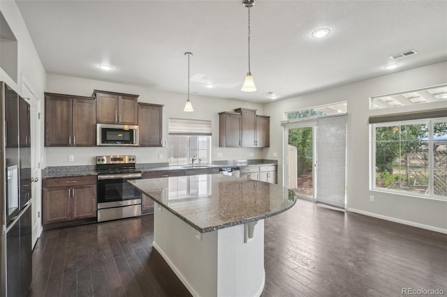 kitchen with appliances with stainless steel finishes, sink, dark stone countertops, a center island, and hanging light fixtures