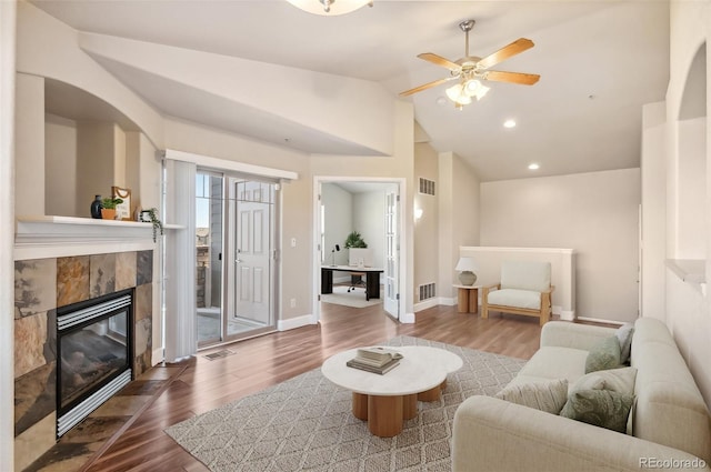 living room featuring wood-type flooring, ceiling fan, lofted ceiling, and a tiled fireplace