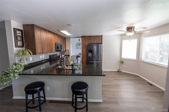 5630 W 115th Ave, Westminster, CO 80020 - kitchen with stainless steel appliances, a peninsula, dark stone counters, brown cabinetry, and a breakfast bar area