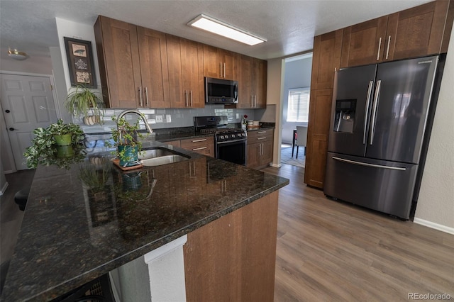 5630 W 115th Ave, Westminster, CO 80020 - kitchen featuring stainless steel appliances, light wood-type flooring, dark stone countertops, tasteful backsplash, and a peninsula