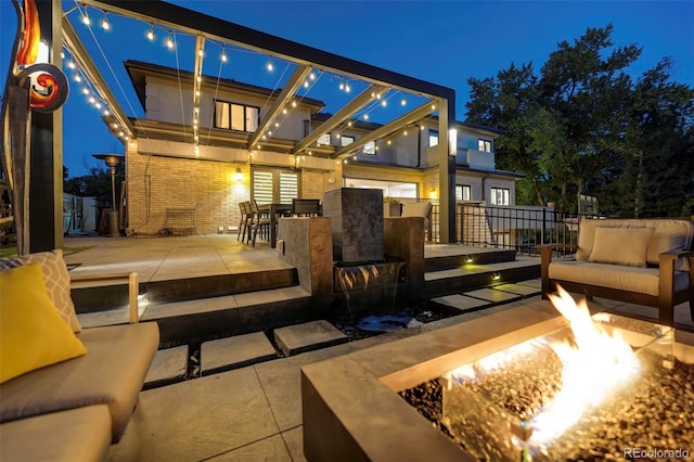 back of house at night with brick siding, an outdoor living space with a fire pit, and a patio