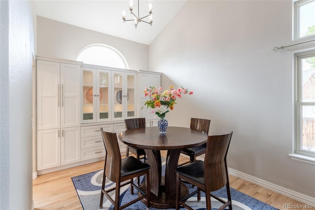 dining space with an inviting chandelier, baseboards, light wood-style flooring, and lofted ceiling