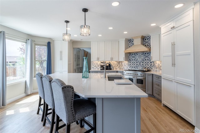 kitchen with range with two ovens, tasteful backsplash, a sink, premium range hood, and light wood-style floors