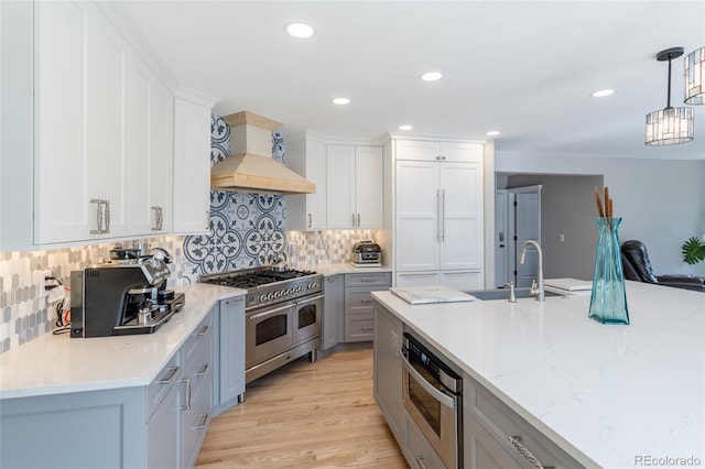 kitchen with hanging light fixtures, premium range hood, tasteful backsplash, and range with two ovens
