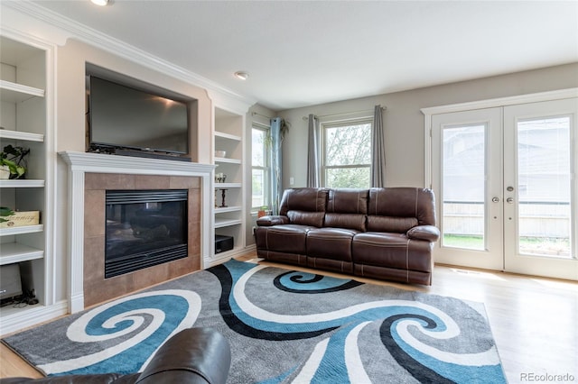 living area featuring french doors, built in shelves, wood finished floors, and a tile fireplace