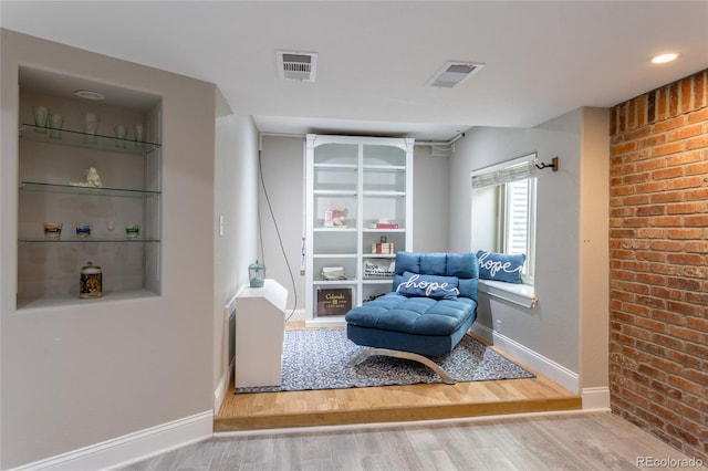 sitting room with baseboards, visible vents, wood finished floors, and brick wall