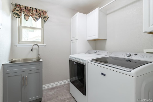 washroom featuring washing machine and clothes dryer, cabinet space, a sink, light wood-style flooring, and baseboards
