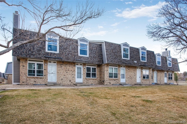 view of front facade featuring roof with shingles, brick siding, a chimney, and a front lawn