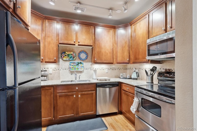 kitchen with decorative backsplash, appliances with stainless steel finishes, light stone counters, sink, and light hardwood / wood-style floors