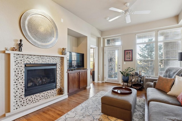 living room featuring a tiled fireplace, ceiling fan, and light hardwood / wood-style floors