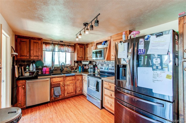 kitchen with sink, a textured ceiling, appliances with stainless steel finishes, tasteful backsplash, and light hardwood / wood-style floors