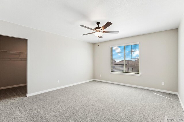 unfurnished bedroom with carpet floors, baseboards, a walk in closet, and ceiling fan