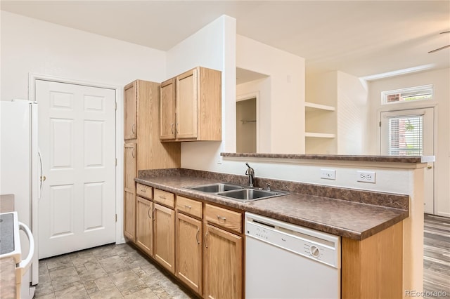 kitchen with dark countertops, a sink, a peninsula, and white appliances