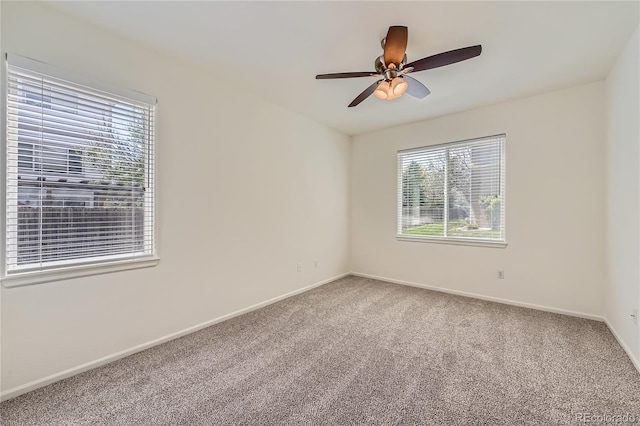 carpeted spare room featuring baseboards and a ceiling fan