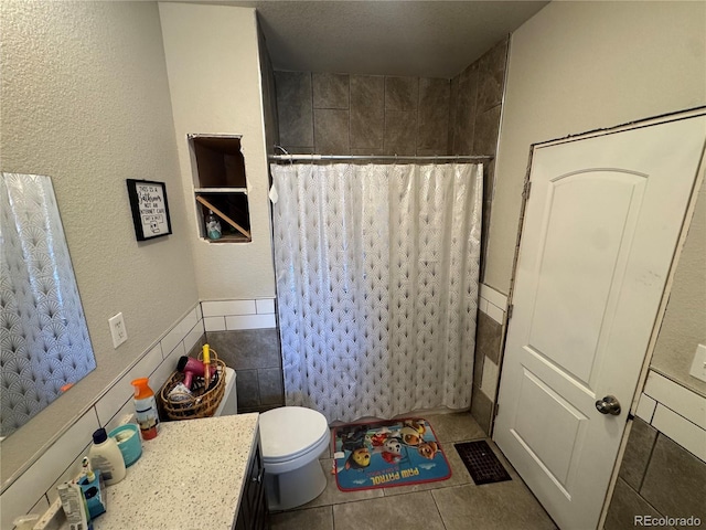 full bathroom with a shower with shower curtain, toilet, a textured wall, vanity, and tile patterned flooring