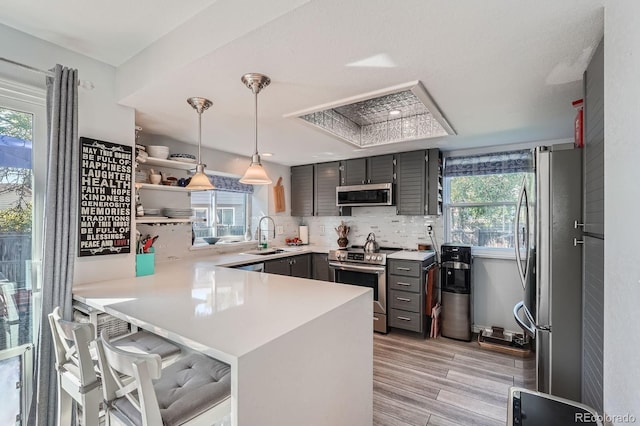 6311 Xavier St, Arvada, CO 80003 - kitchen featuring stainless steel appliances, a peninsula, gray cabinets, light wood finished floors, and backsplash