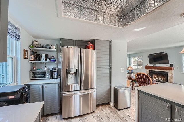 6311 Xavier St, Arvada, CO 80003 - kitchen featuring stainless steel fridge, light countertops, light wood-style floors, gray cabinets, and a fireplace