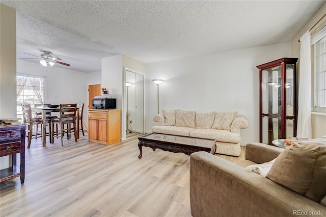 living room with a textured ceiling, light hardwood / wood-style floors, and ceiling fan